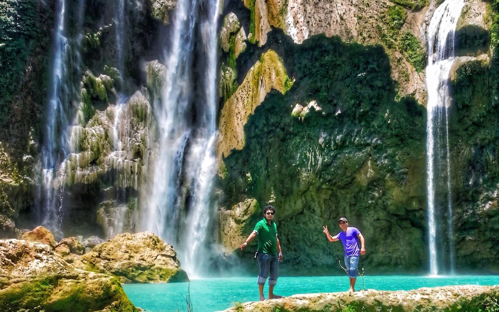 Dos personas saludando al pie de la Cascada del Meco — agua turquesa