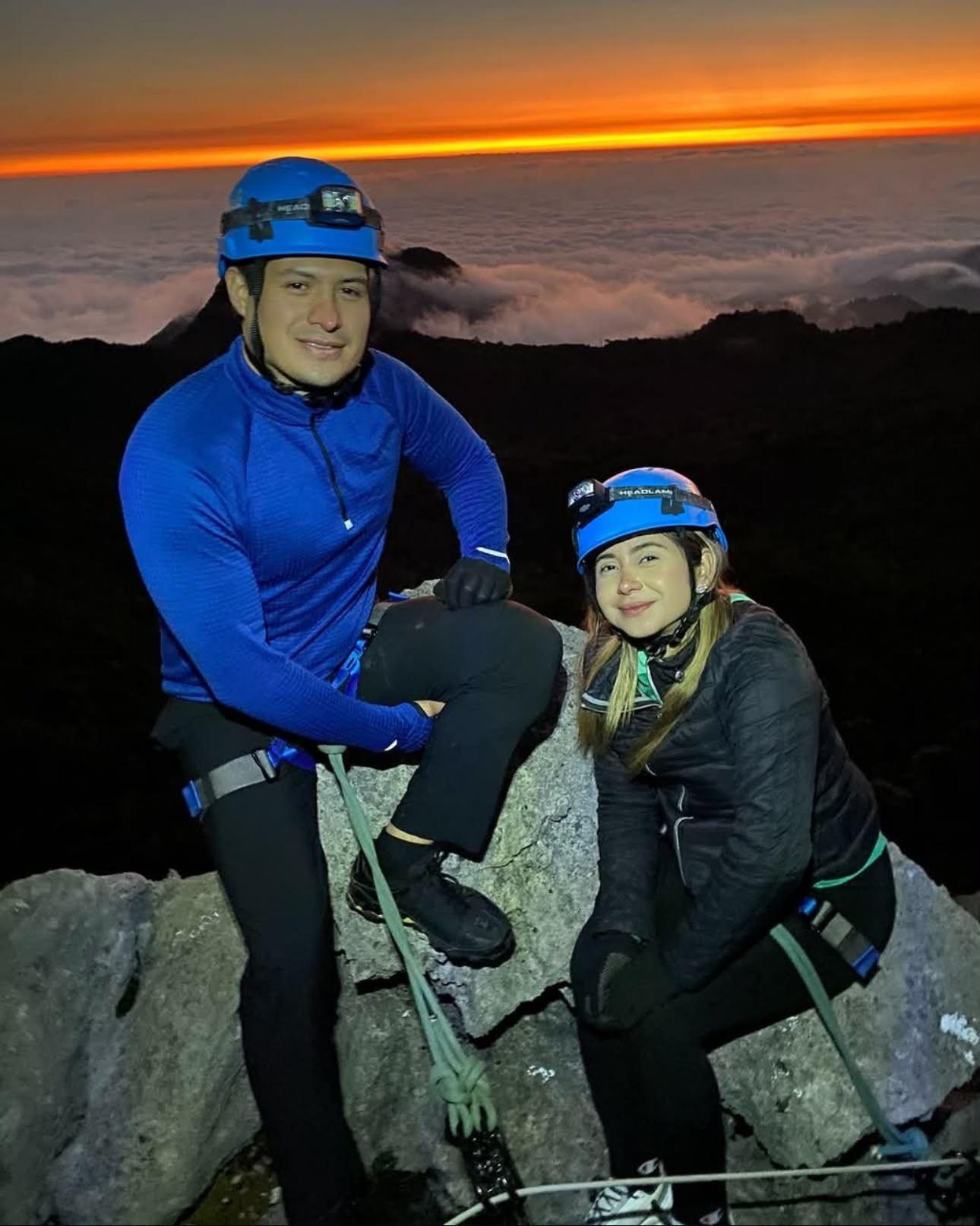 Couple resting on the summit rocks with the orange band of the sunrise behind them