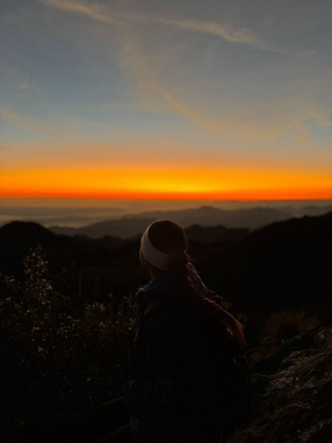 Hiker with a backpack, seen from behind, watching the day break from the summit trail