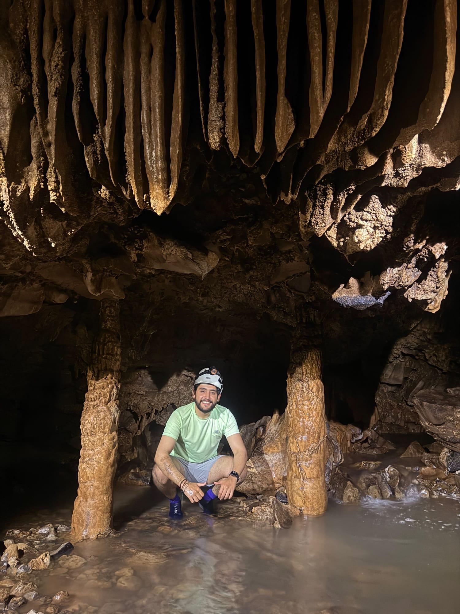 Xilo Cave — crouching between two columns, ankle-deep in water