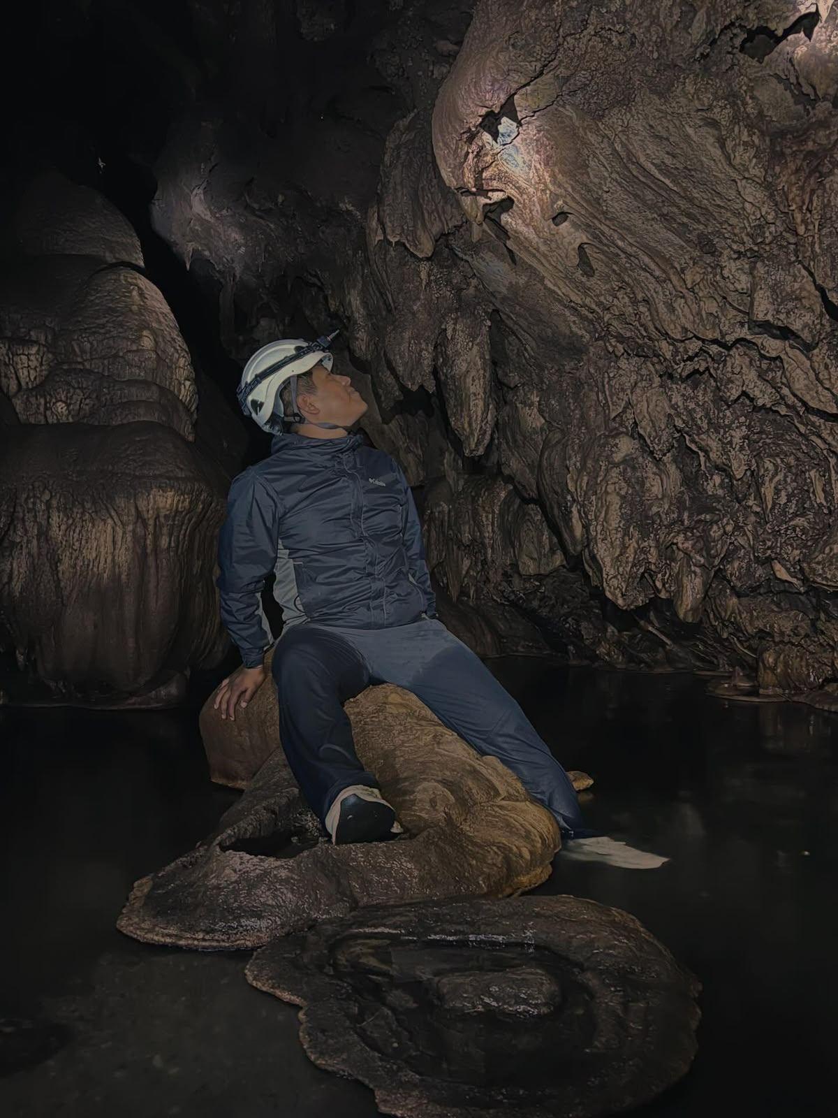 Visitante sentado sobre una formación rocosa mirando la bóveda de la gruta, iluminado solo por su lámpara