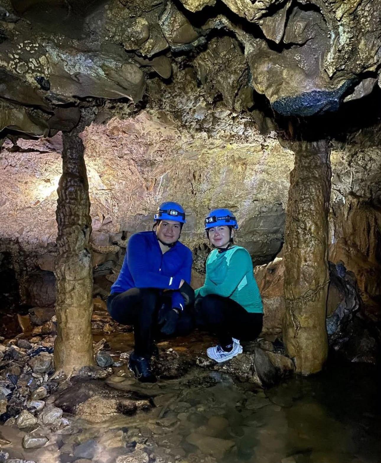 Pareja con casco en cuclillas entre dos columnas de piedra formadas gota a gota dentro de la gruta