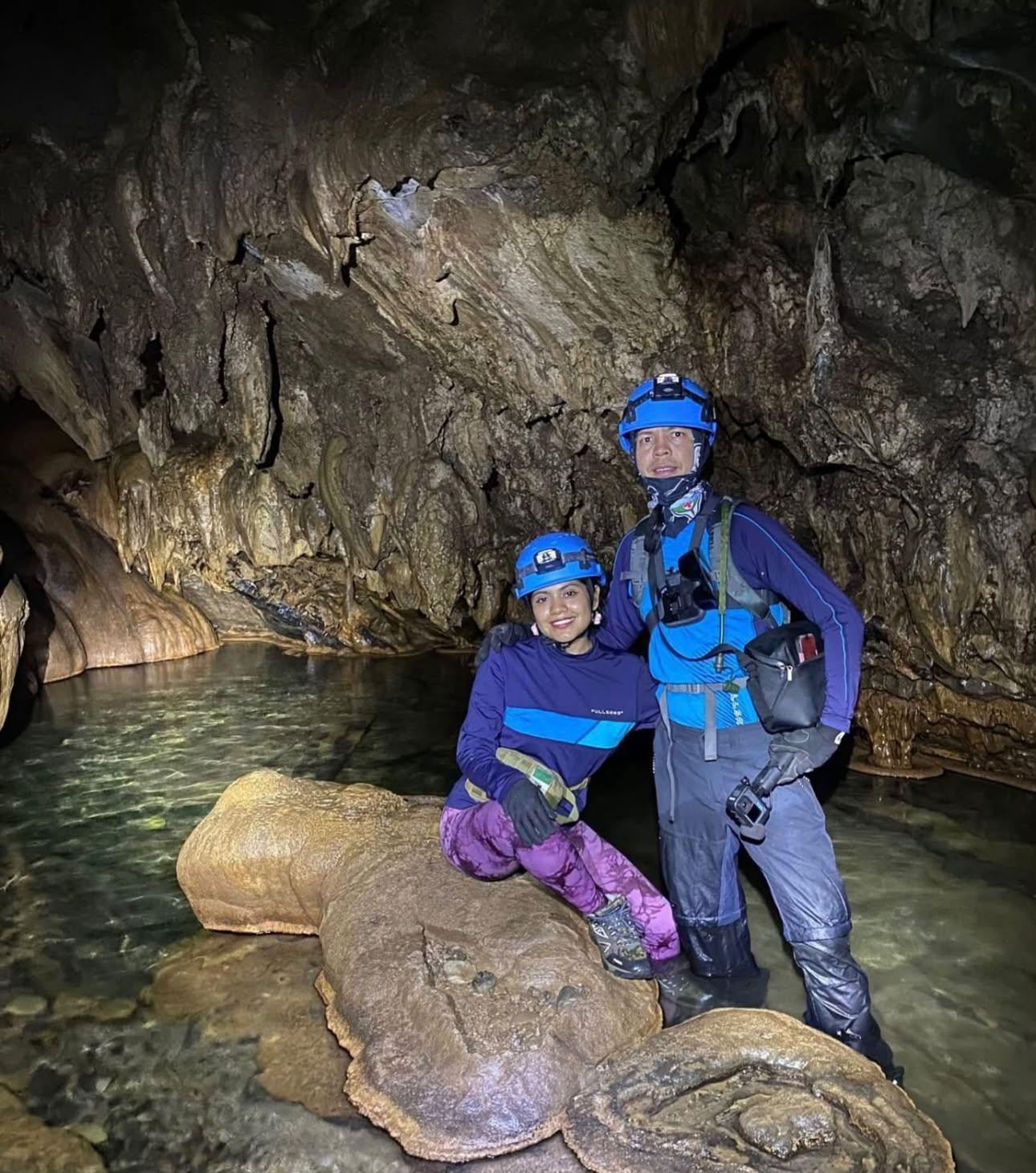 Guía y visitante de pie sobre una colada de piedra en el agua, al fondo de la Gruta de Xilo