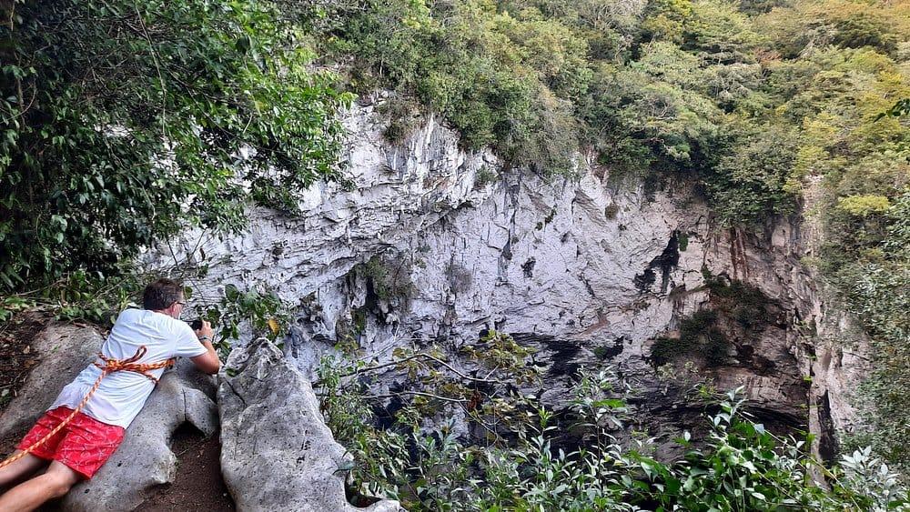Sótano de las Huahuas — viajero asomado al borde del abismo, asegurado con cuerda