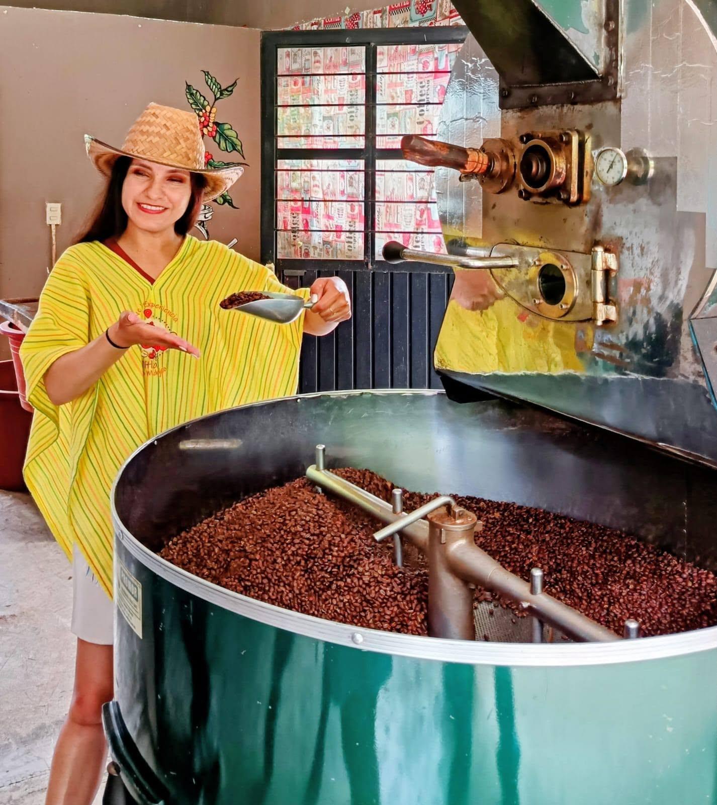 Host in a yellow poncho showing a scoop of freshly roasted beans over the cooling drum
