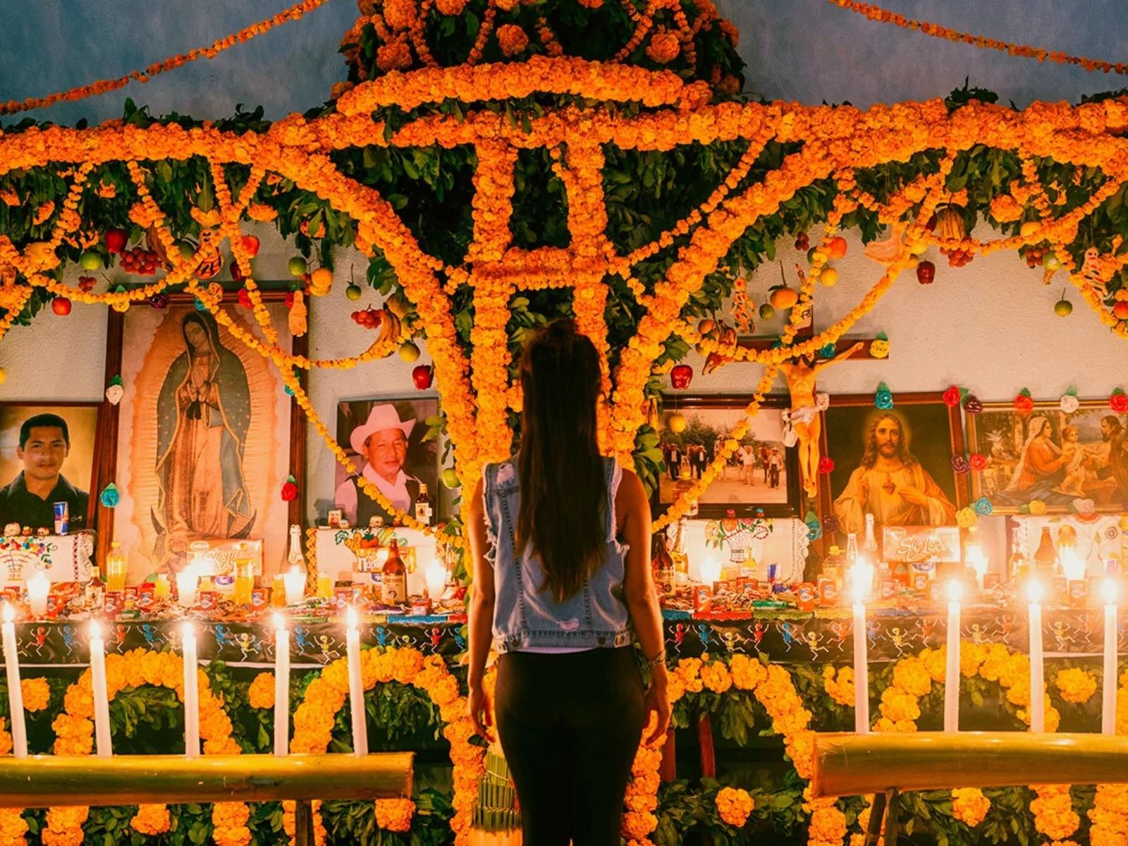 Mujer de espaldas frente a un altar de Xantolo con arcos de cempasúchil y velas encendidas