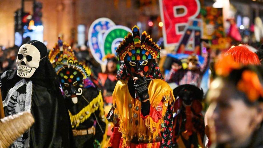 Comparsa de Xantolo de noche: danzantes con máscaras, una calavera y trajes de colores en pleno desfile