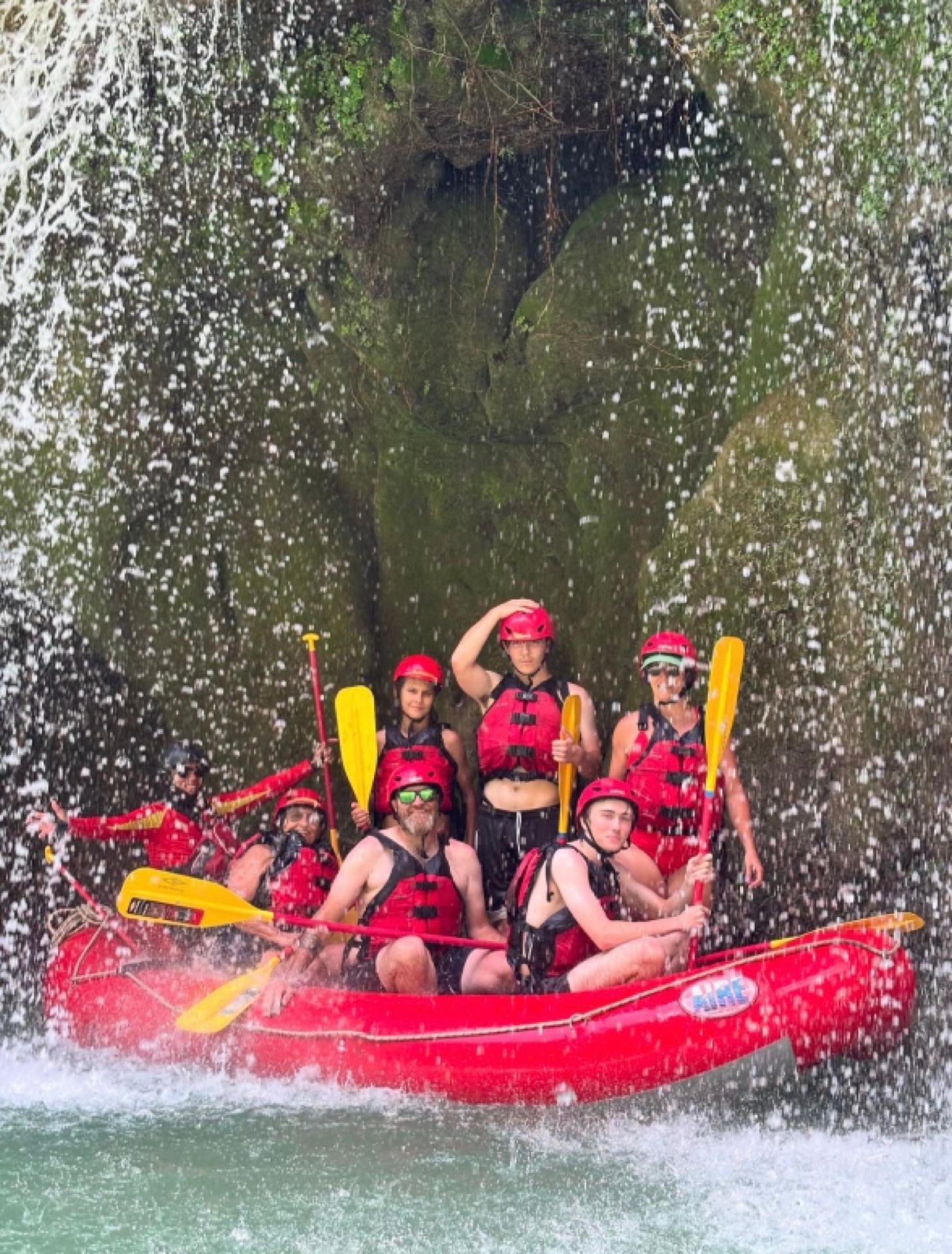 Balsa roja con su tripulación posando bajo la cortina de una cascada en el Río Tampaón