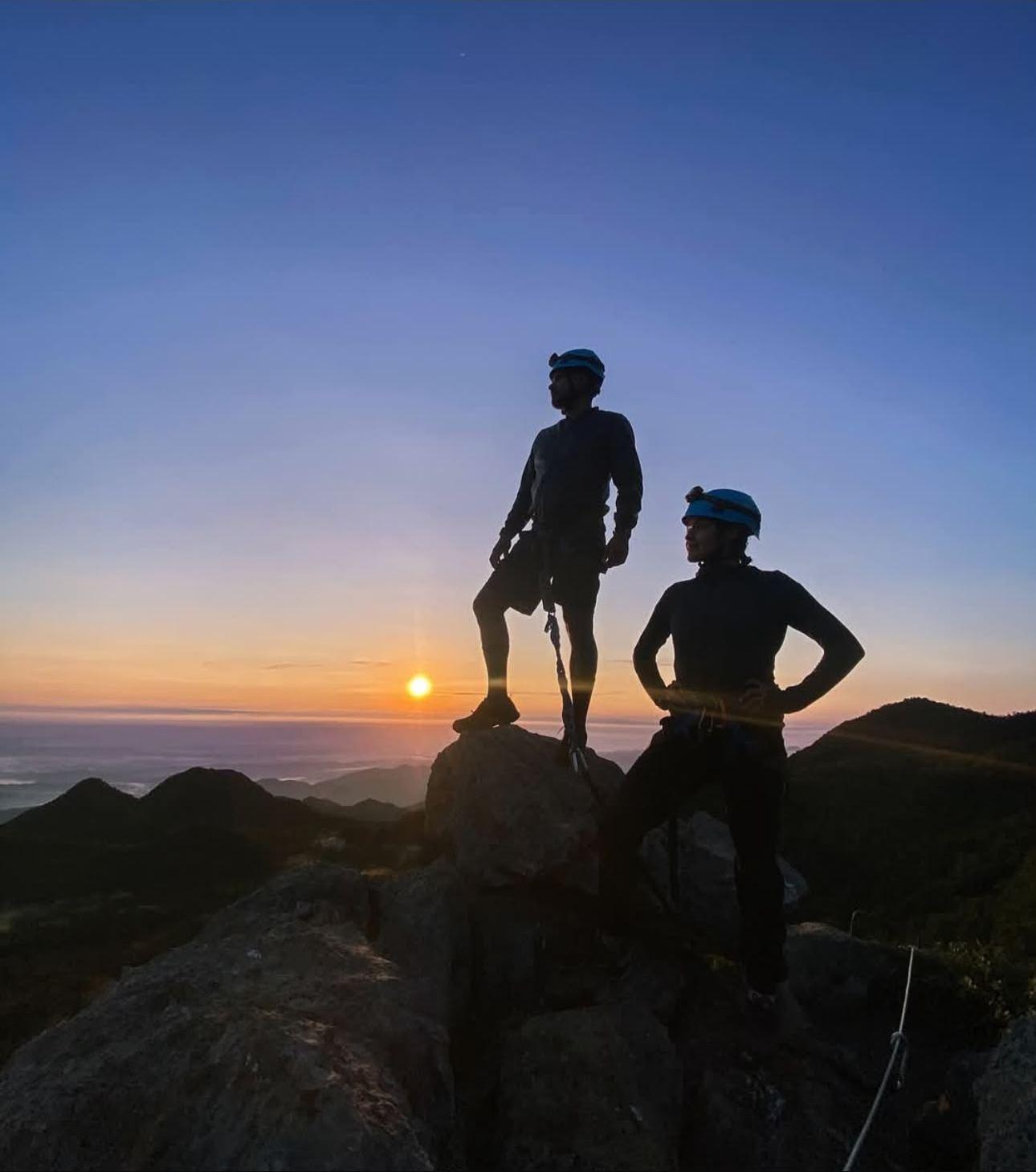 Dos siluetas de pie sobre la roca más alta del Cerro del Pilón, recortadas contra el sol que sale