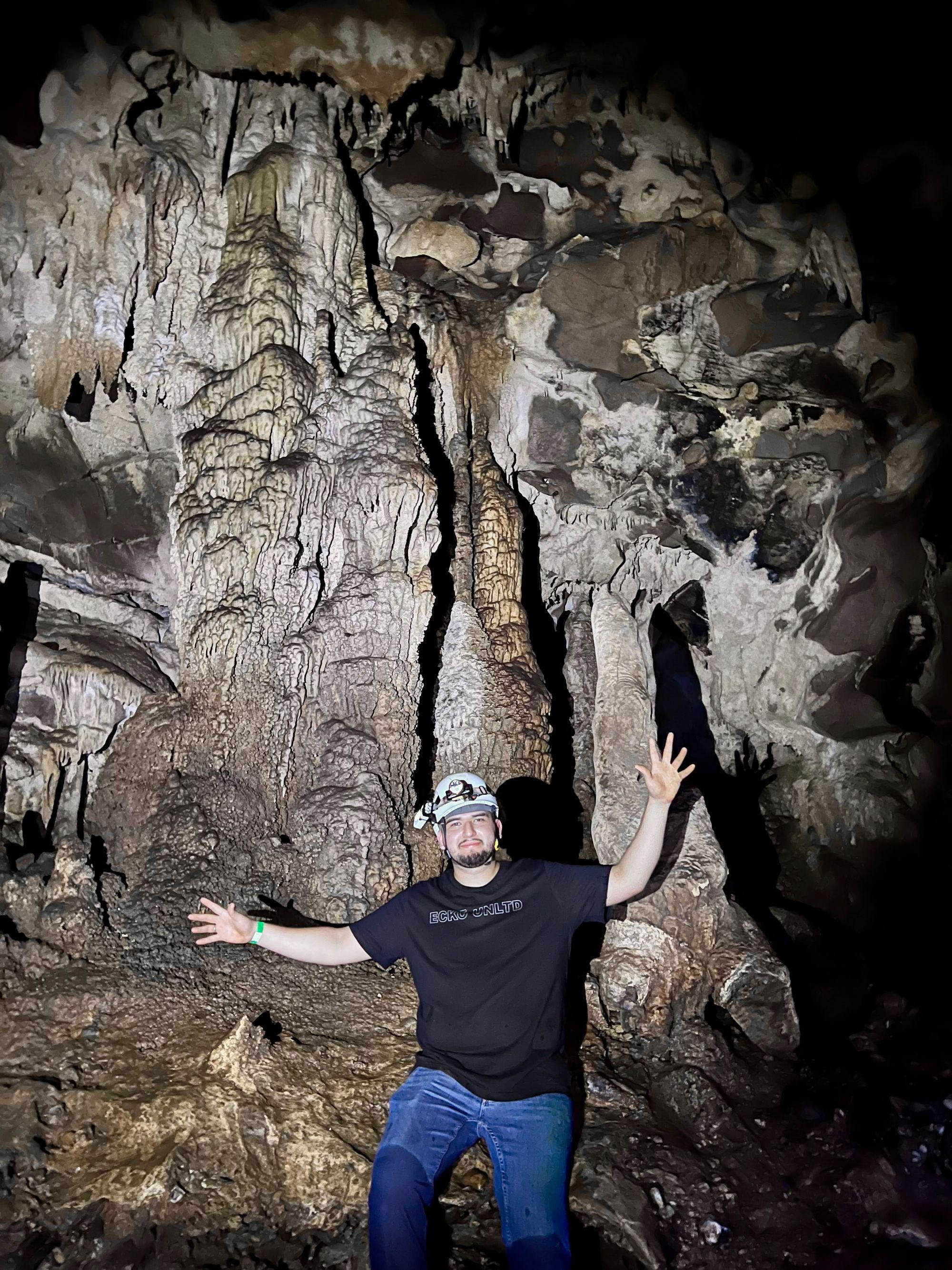 Visitante con los brazos abiertos frente a las columnas de la Gruta de Xilo, que lo superan varias veces en altura