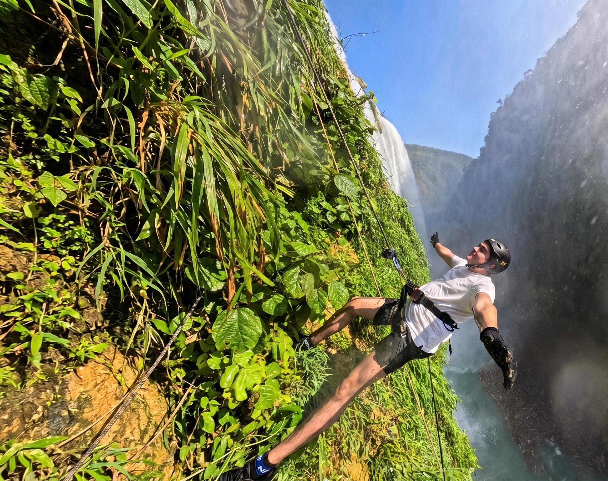 Aventurero recostado en el arnés mirando hacia arriba durante el descenso en rappel frente a la Cascada de Tamul