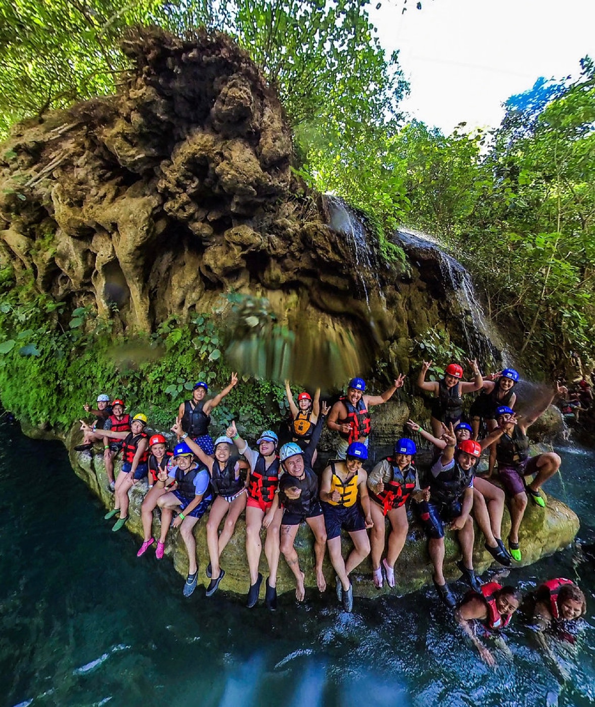 Grupo de viajeros con chalecos salvavidas sobre una roca junto a una cascada en la selva potosina