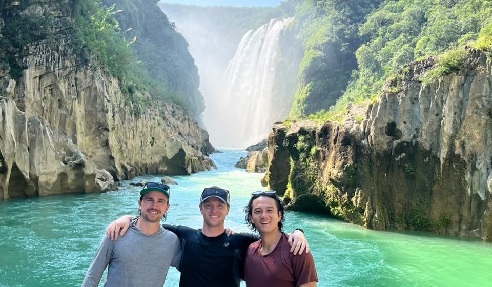 Tres amigos sobre una roca del Río Tampaón con la Cascada de Tamul detrás y el agua turquesa