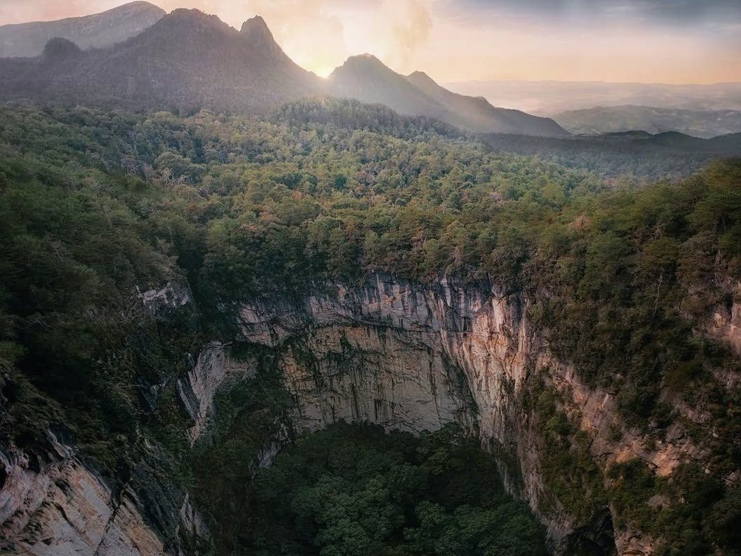 La Olla de la Luz vista desde el borde: un sótano de paredes de roca con bosque en el fondo y la sierra de Xilitla al amanecer