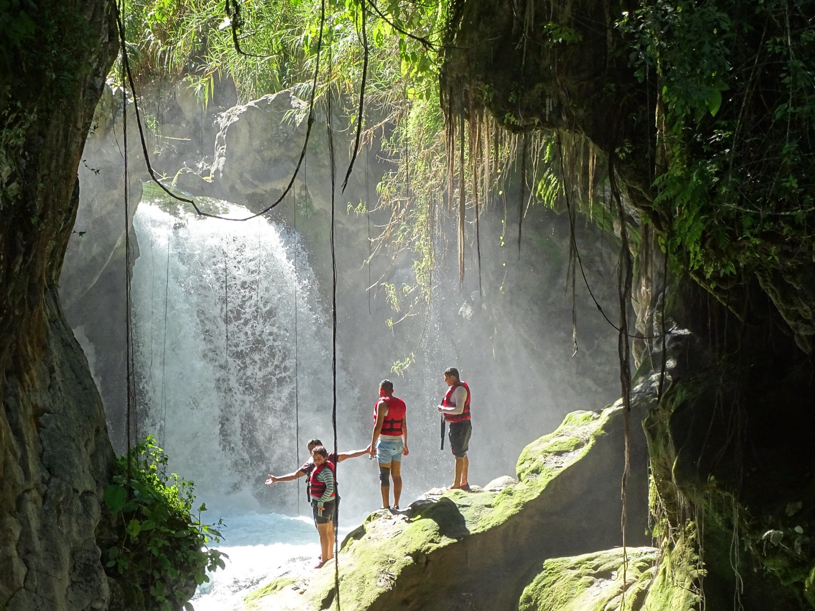 Cascada del Puente de Dios en Tamasopo iluminada por rayos de luz dentro de la cueva, con visitantes en las rocas