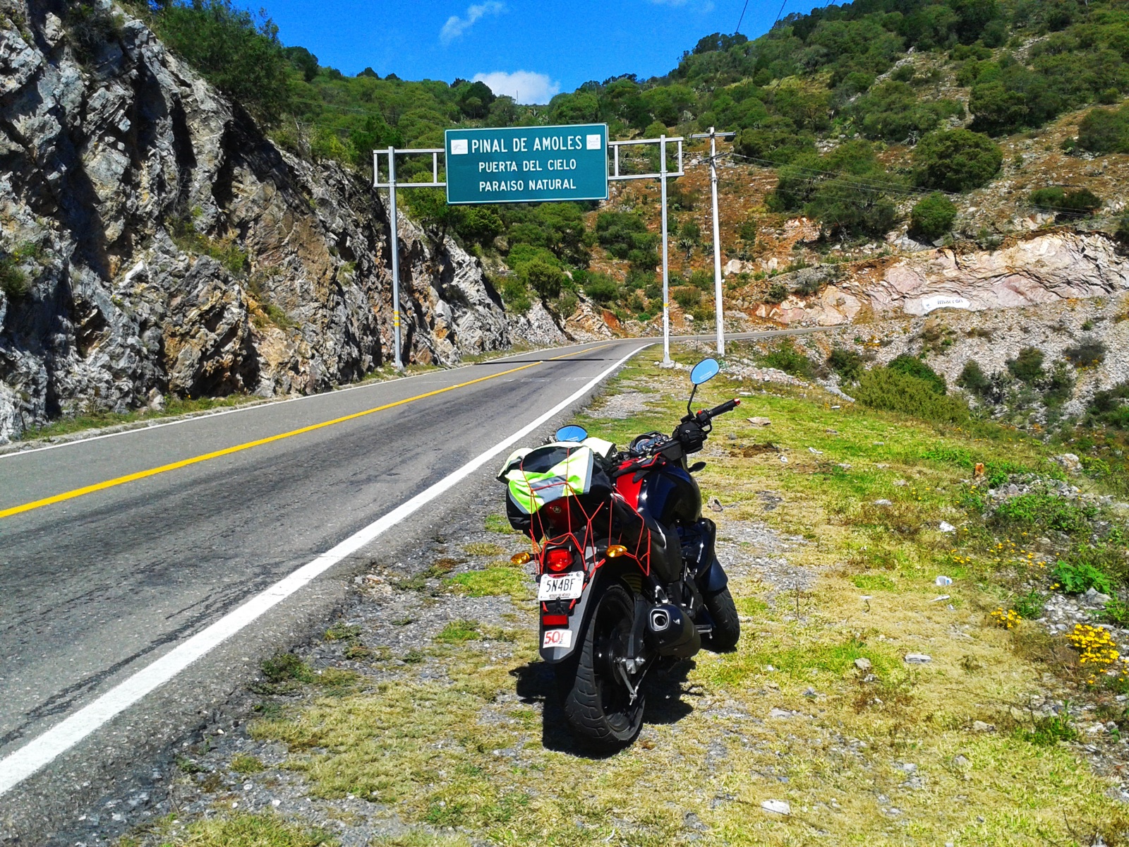 Carretera de montaña hacia la Huasteca Potosina con motocicleta y señalización vial bajo cielo despejado