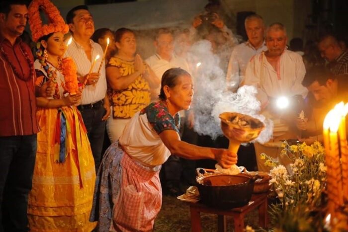 Mujer ofreciendo humo de copal con un sahumerio de barro frente a un grupo con velas encendidas durante una velación de muertos
